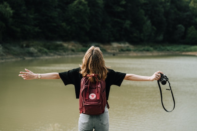 Woman wearing a backpack and standing next to a lake with her arms spread to symbolize overcoming the fear of the unknown