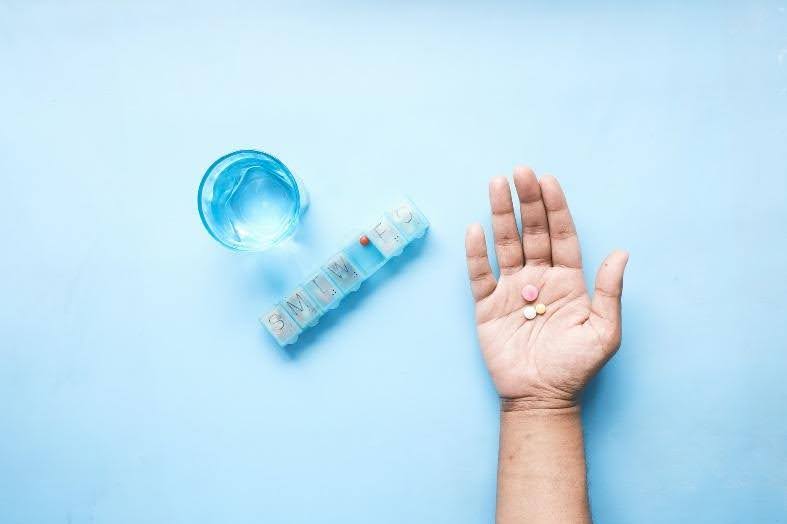 A hand next to a medication container.