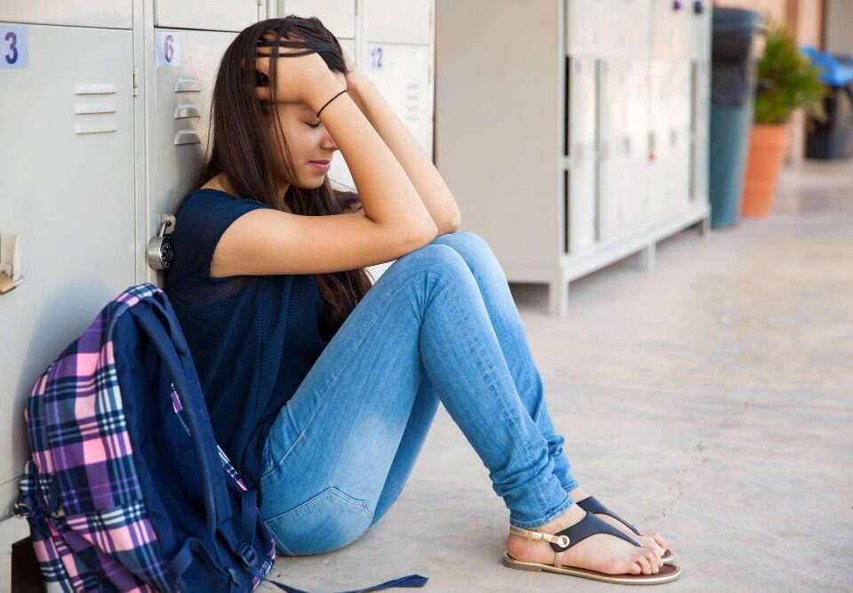 teenage girl sitting at lockers with her head in her hands